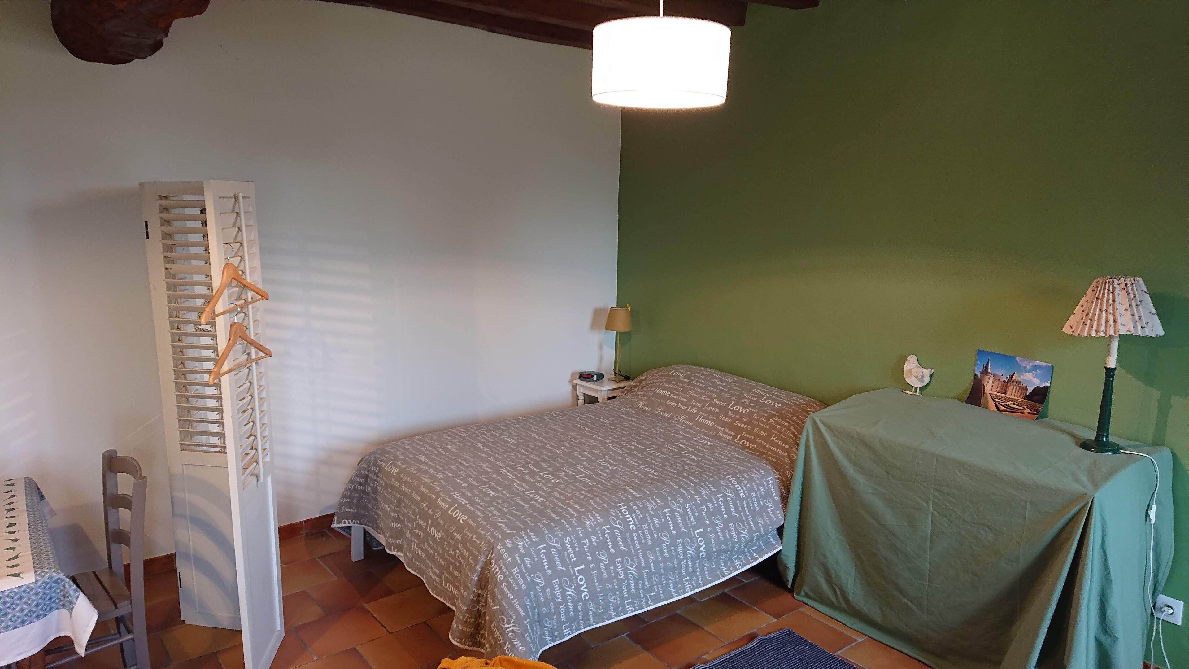 Un dormitorio con cama, mesita de noche, lámpara, silla y perchero.