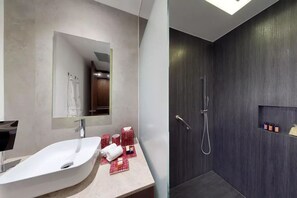 A modern bathroom with a large white sink, a mirror, and a shower area with dark wood paneling.