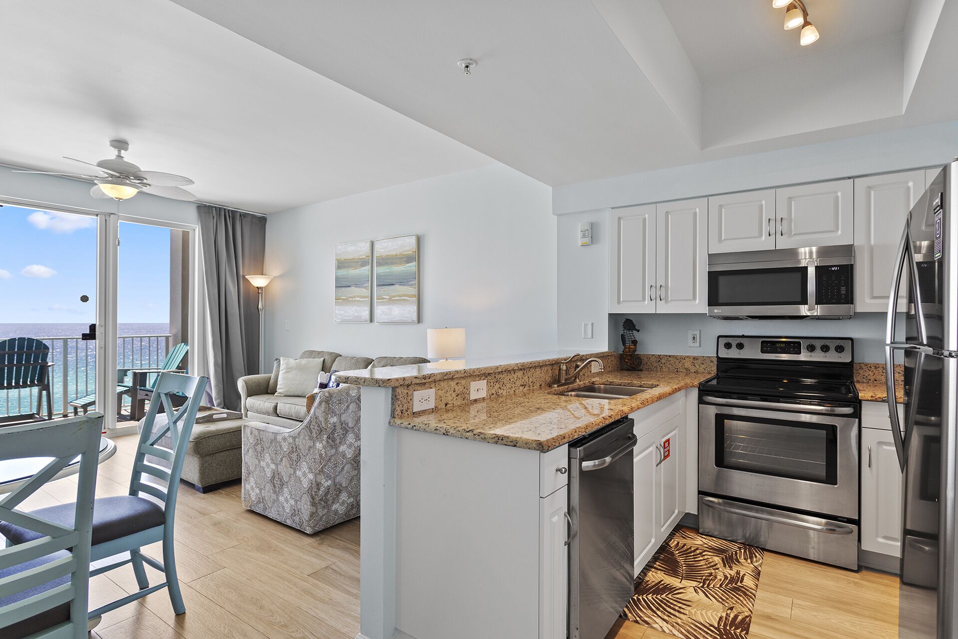 A modern kitchen with stainless steel appliances, a granite countertop, and a view to the ocean.