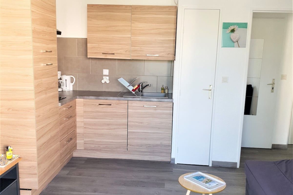 A modern kitchen with wooden cabinets, a sink, and a small table with a magazine.