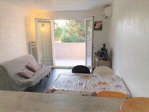 Una habitación pequeña y bien iluminada con una cama, un escritorio y una silla. Hay una puerta corrediza de vidrio que da a un espacio al aire libre.