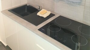 A kitchen with a black sink, a stove, and a window with sheer curtains. - Les Jardins Du Golf - Mandelieu (Mandelieu-La-Napoule)