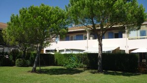 A two-story building with a white facade and blue windows. There are two trees in the foreground, and a well-maintained lawn. - Les Jardins Du Golf - Mandelieu (Mandelieu-La-Napoule)