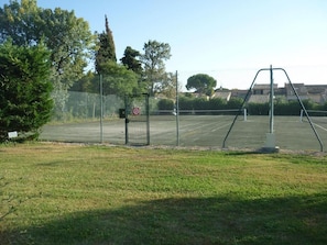 Un court de tennis entouré d’une clôture, avec un filet, une balançoire et un panneau indiquant qu’il est interdit de fumer.