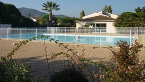 A swimming pool with a white fence, surrounded by greenery and a building with a tiled roof. - Les Jardins Du Golf - Mandelieu (Mandelieu-La-Napoule)