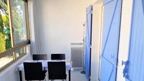 A narrow corridor with a table and chairs, a window, and blue doors. - Les Jardins Du Golf - Mandelieu (Mandelieu-La-Napoule)