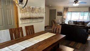 A dining area with a wooden table set for four, a chandelier, and a painting of trees on the wall.