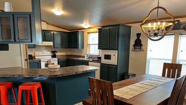 A modern kitchen with dark cabinets, a central island, red bar stools, and a dining table with chairs.