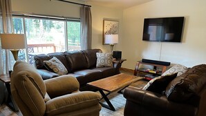 A living room with a brown leather sofa, a wooden coffee table, and a TV mounted on the wall.