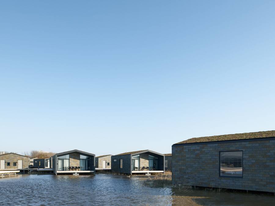 A modern waterfront property with multiple buildings, some with glass facades and others with brick exteriors, situated along a calm body of water.