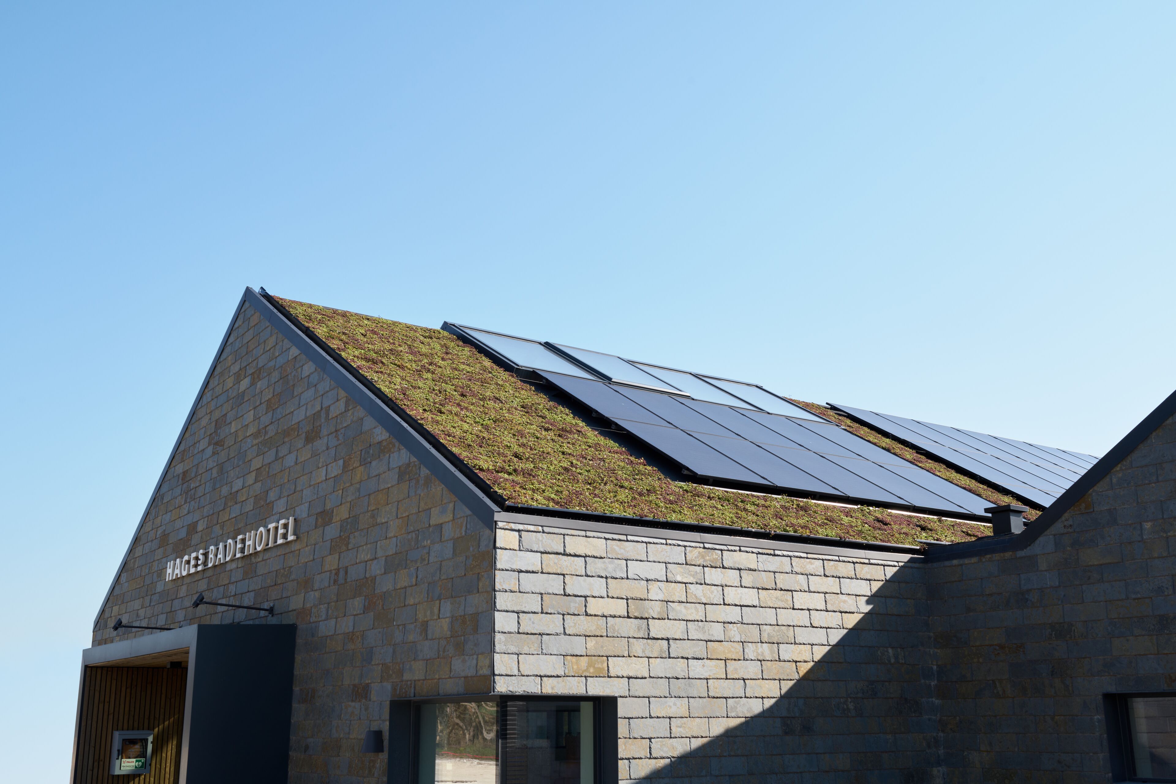 A building with a sloped roof featuring solar panels and a green roof.