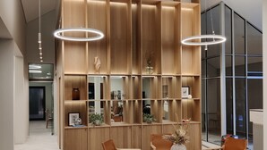 A modern interior with a central wooden shelving unit, a round table with chairs, and pendant lighting.