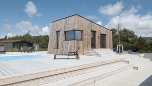A modern wooden house with a pool, outdoor seating, and a staircase leading to the entrance.