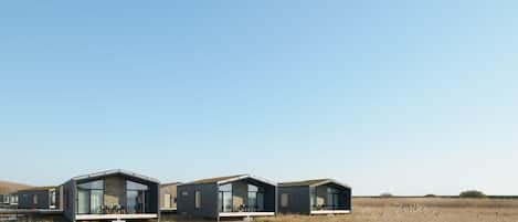 A row of modern, minimalist houses with large glass windows, situated by a calm water body.