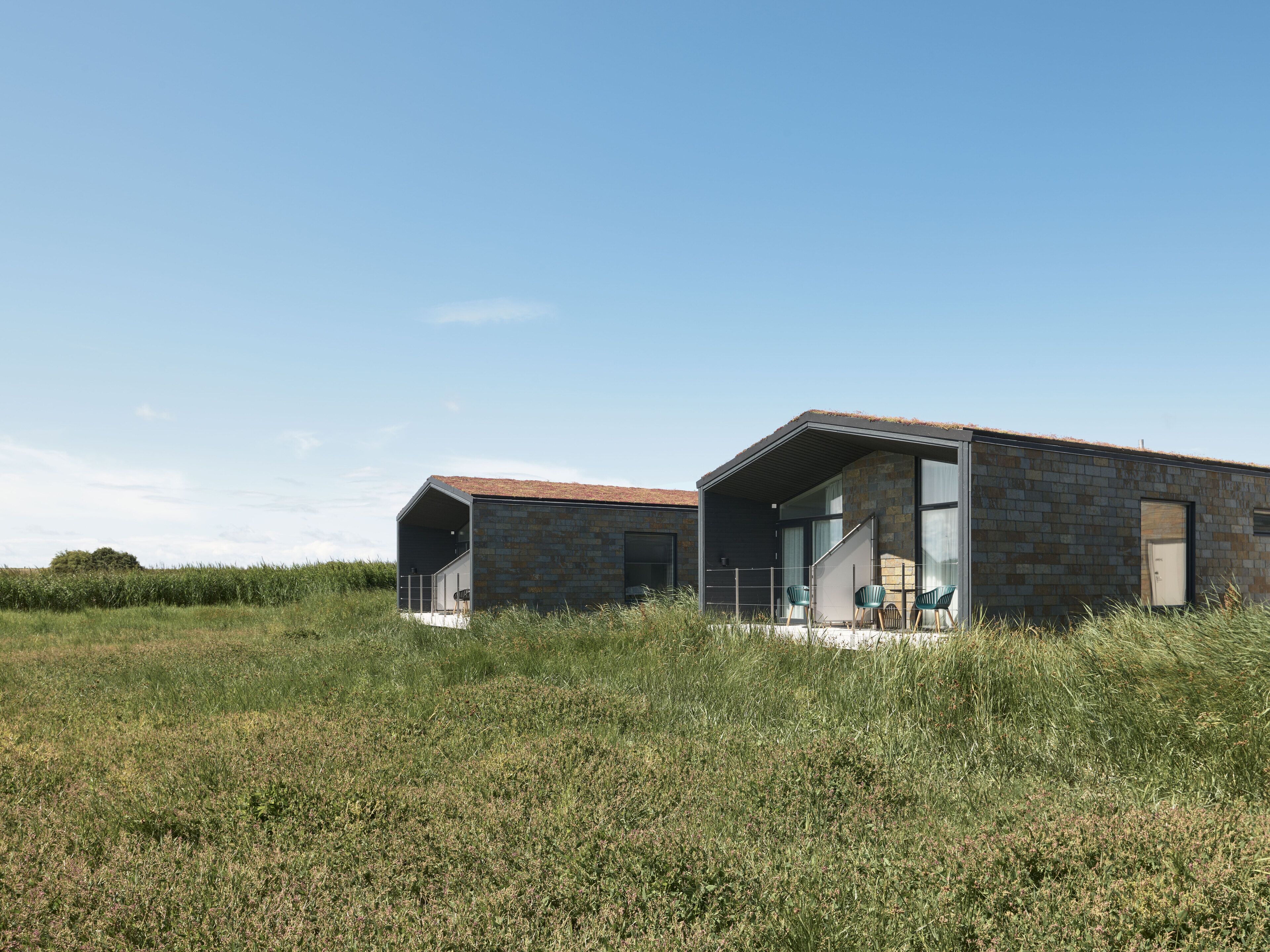 Una casa moderna con fachada de piedra y amplios ventanales, ubicada en un campo cubierto de hierba.