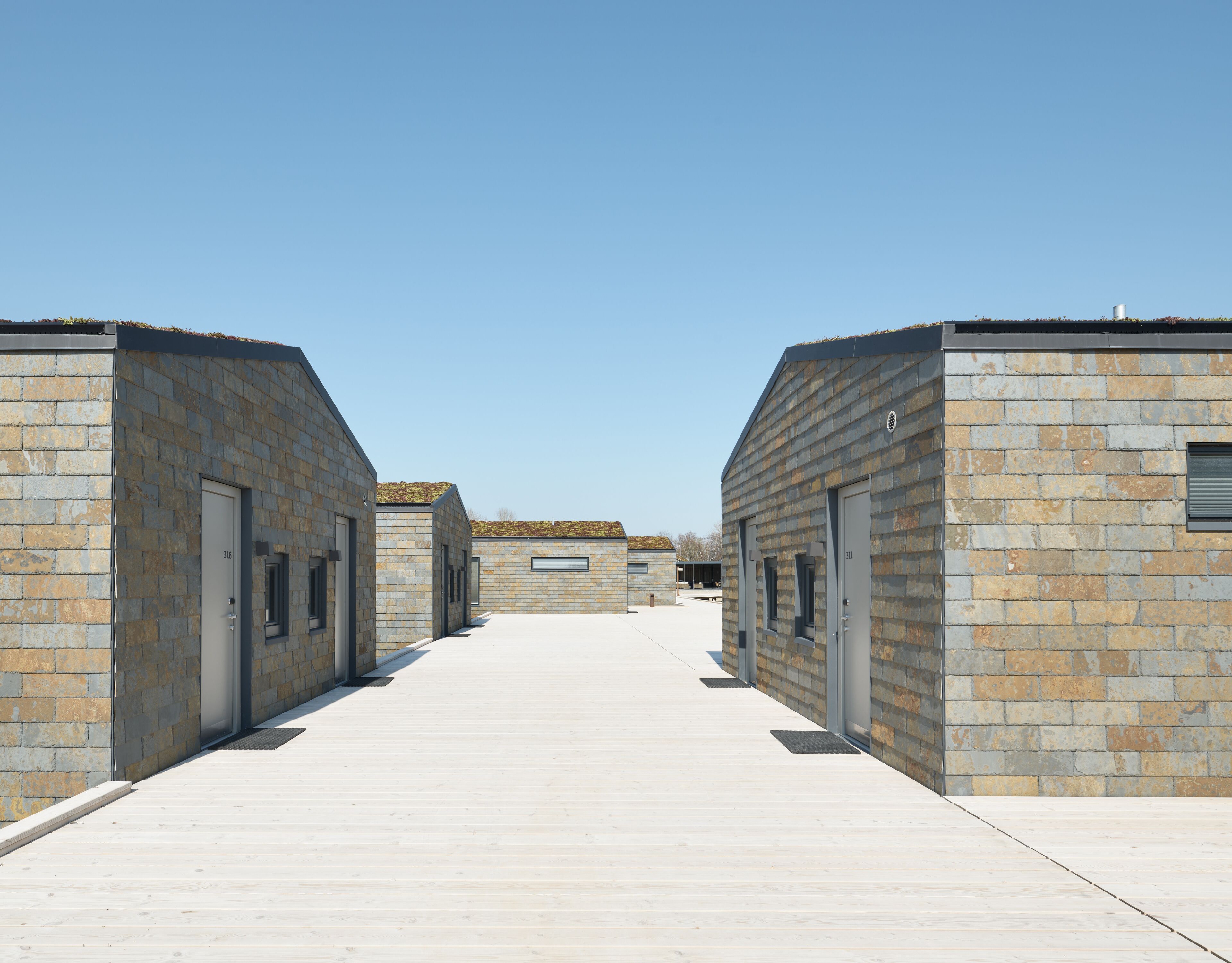 Una hilera de edificios modernos revestidos de piedra, con puertas y ventanas amplias, unidos por un paseo ancho y llano.