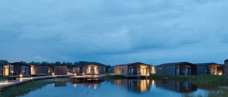 Varias cabañas modernas y bien iluminadas junto a un lago tranquilo al anochecer.