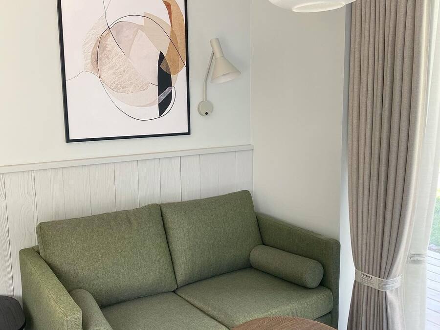 A modern living room with a green sofa, a round wooden coffee table, a white pendant light, and a framed abstract artwork on the wall.