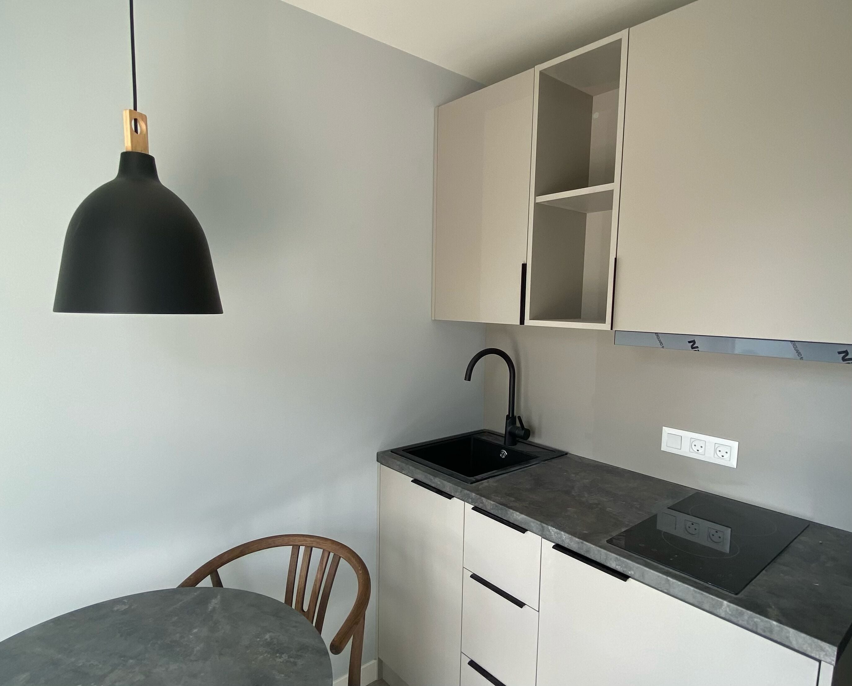 A compact kitchen with a black pendant light, a single sink, and a wooden chair.