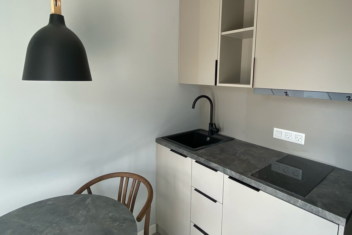A compact kitchen with a black pendant light, a single sink, and a wooden chair.