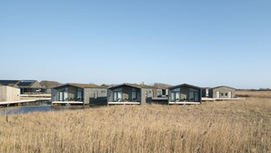 A row of modern, single-story cabins with large windows, situated in a natural, grassy area.