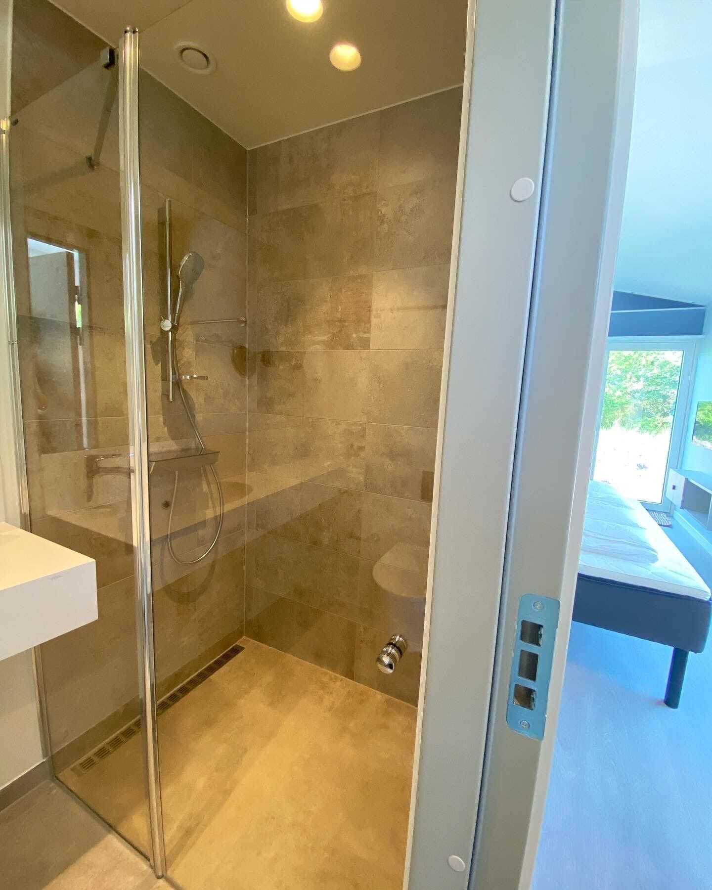 Un bagno moderno con doccia vetrata, lavandino bianco e water a vista.
