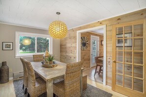 A dining area with a wooden table, wicker chairs, and a hanging light fixture.