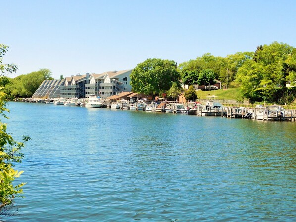 A marina with boats docked, a large building with multiple balconies, and lush greenery in the background.