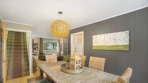 Un coin repas avec une table en bois, des chaises en osier, un luminaire suspendu et une œuvre d’art accrochée au mur.