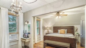 Une chambre à coucher avec un lit en bois, un banc, un lustre, un ventilateur de plafond et une fenêtre avec des stores.