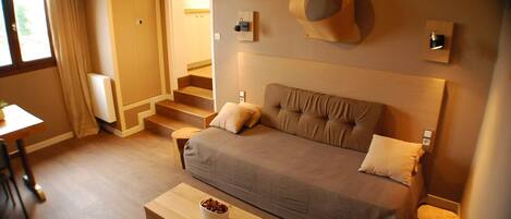 Une chambre confortable avec un canapé, une petite table sur laquelle se trouve un bol, et un escalier menant à une autre pièce.