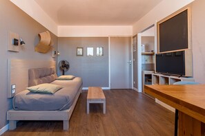 Una habitación pequeña con cama, una mesita de madera, escritorio, televisión y una puerta que da a otra habitación.