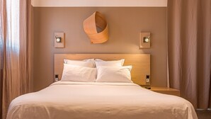 Et hotelværelse med en stor seng, et træsengegærde, to sengeborde og vægmonterede lamper.