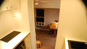 Et kompakt køkken med et indbygget komfur, en lille skammel og et spiseområde med bord og stole.