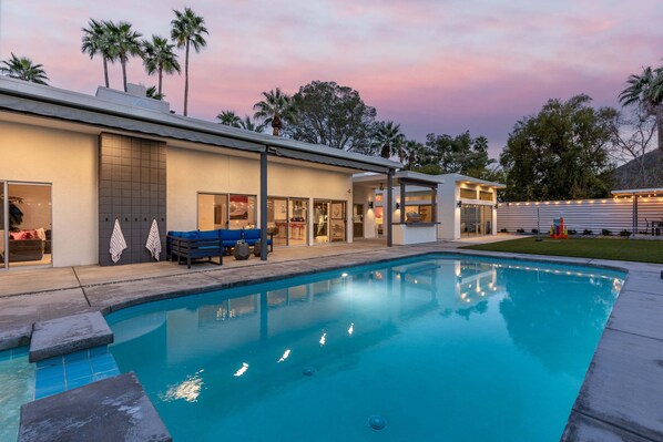 A modern building with a swimming pool, outdoor seating, and palm trees.
