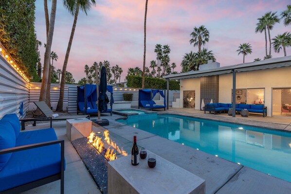 A poolside area with a fire feature, lounge chairs, and a modern building with a glass facade.