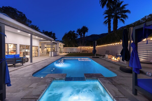 A swimming pool with a hot tub, outdoor seating, and a well-lit patio area.