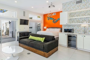 A modern hotel room with a sofa, a bed, a dining area, and a kitchen area.