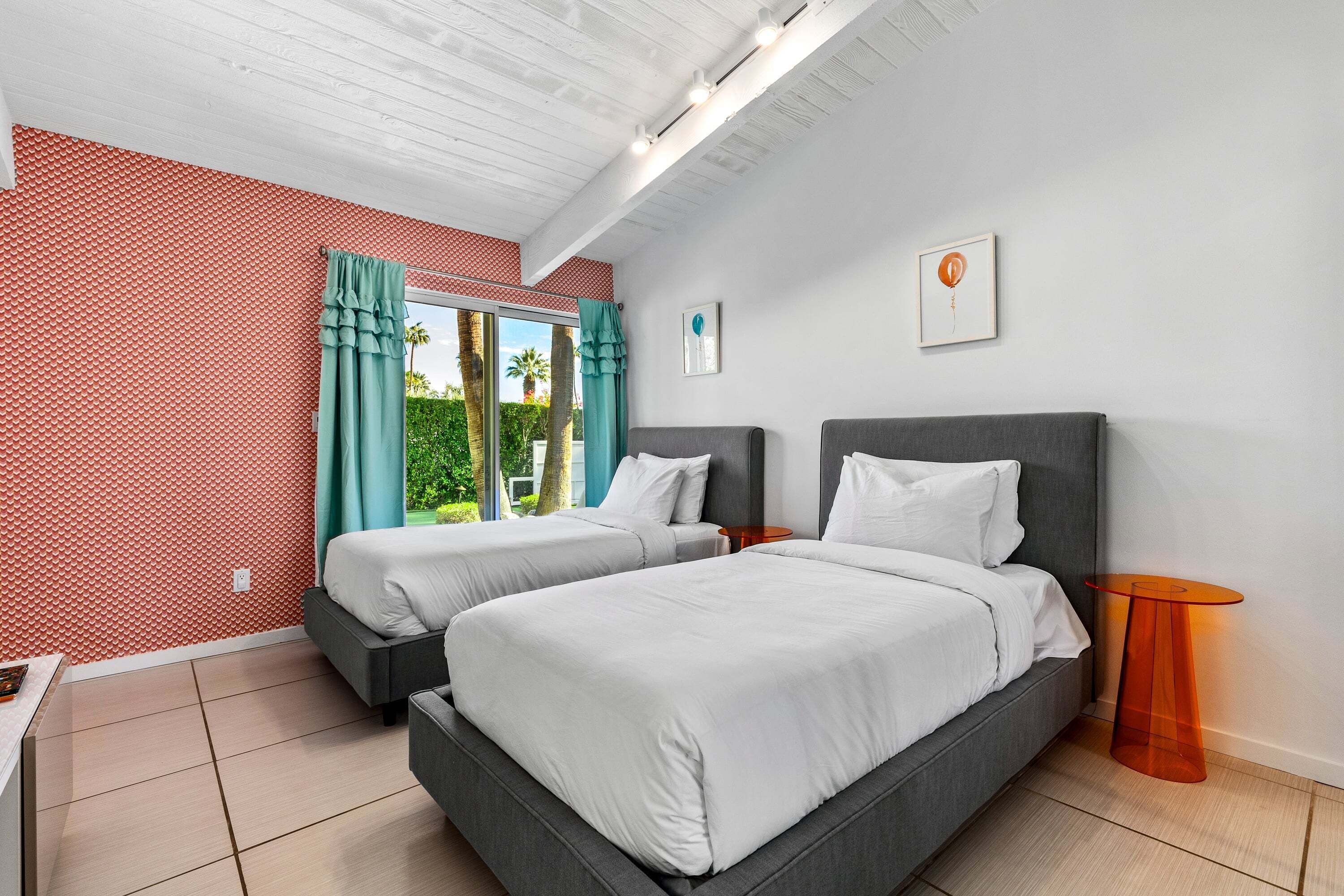 A hotel room with two beds, a small table, and a window with curtains.