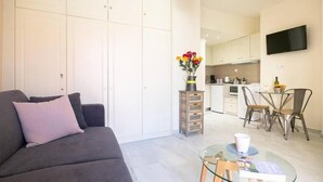 A modern apartment with a grey sofa, a glass coffee table, a kitchen area with a dining table and chairs, and a TV mounted on the wall. - Melina Apartments (Chania)