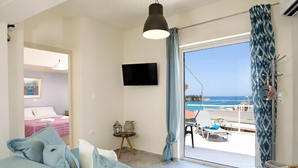 A modern room with a large bed, a TV, a balcony with a view of the sea, and a dining area. - Melina Apartments (Chania)