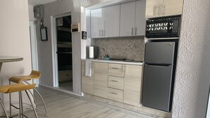 Une cuisine moderne avec des meubles de couleur bois clair, un réfrigérateur en acier inoxydable et un coin bar avec des tabourets.