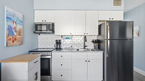 A compact kitchen with white cabinets, a stainless steel refrigerator, a microwave, a coffee maker, and a sink. - Madeira Beach Getaway – Tropic Breeze 7 Pool View Condo (Madeira Beach)