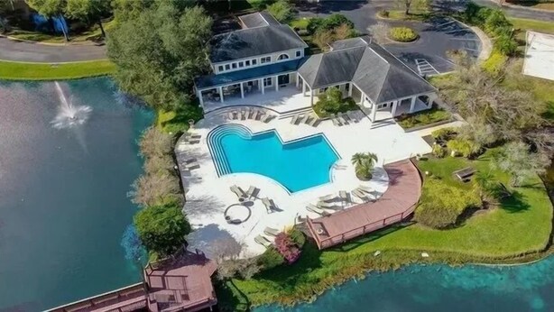 Une grande maison avec une piscine, entourée de verdure et bordée d’un plan d’eau.