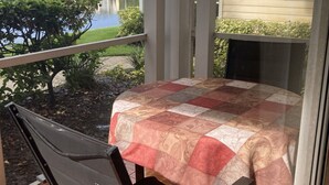 Un balcon avec une table recouverte d’une courtepointe, une chaise et une vue sur un immeuble et une étendue d’eau.
