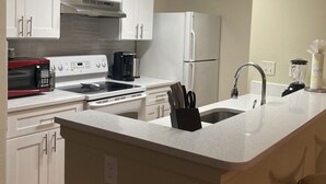 Une cuisine moderne avec des armoires blanches, une cuisinière encastrée, un four à micro-ondes, un réfrigérateur et un grand îlot central doté d’un évier.