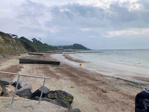 A beach with a rocky shoreline, a pier extending into the water, and a grassy hill in the background.