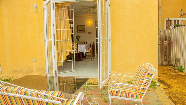 An open patio with a glass table and striped chairs, a dining area visible through the open door, and a wooden fence in the background. - HOLIDAYS AT MANGO WALK COUNTRY CLUB (Montego Bay)