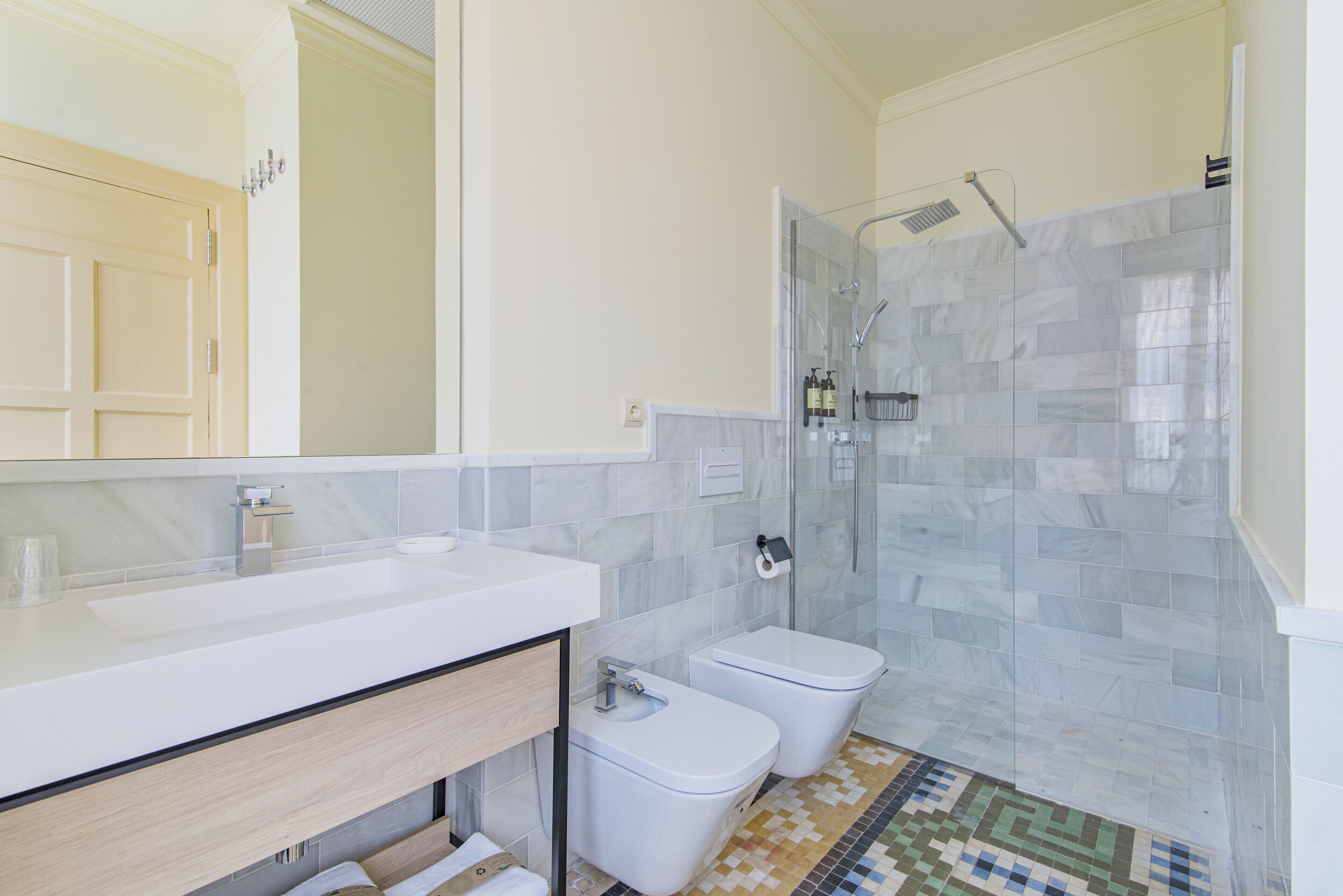 Une salle de bain moderne avec un grand miroir, un lavabo blanc, des toilettes et un espace douche.