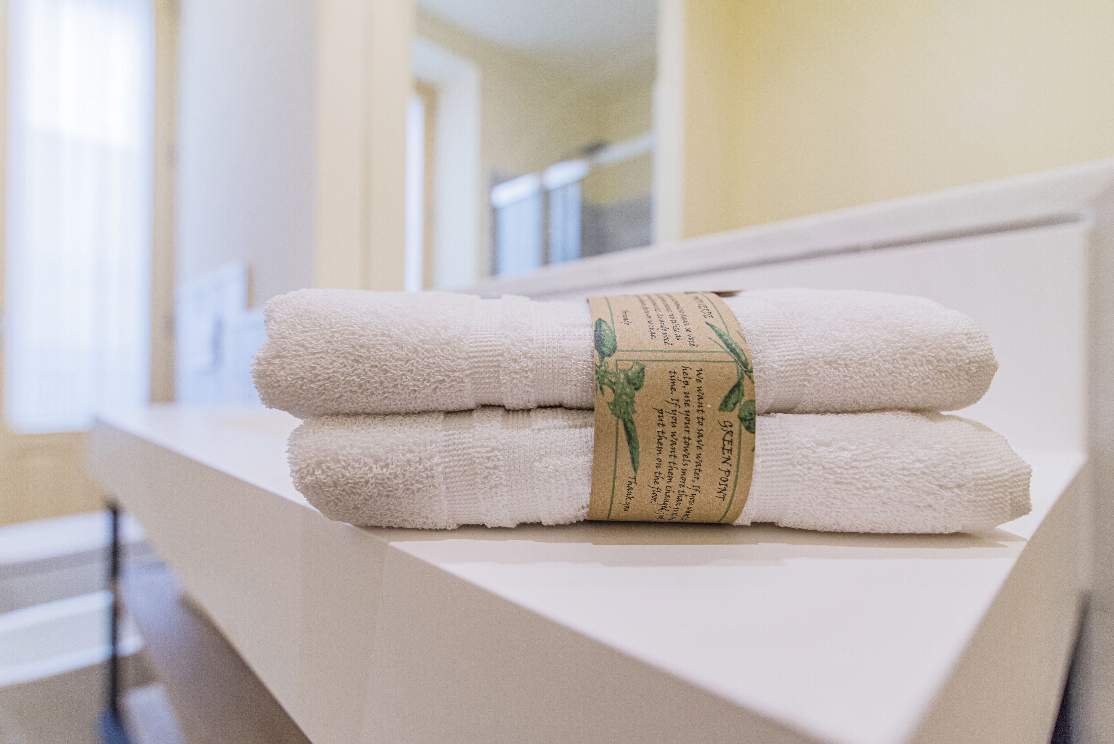 Ein Stapel weißer Handtücher mit einem grünen Etikett auf einer weißen Ablage im Badezimmer eines Hotels.